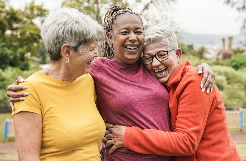 Three mature women hugging each other and having fun outside on a nice day with trees behind them