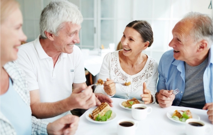 Two mature adult couples enjoying lunch and coffee while talking and laughing.