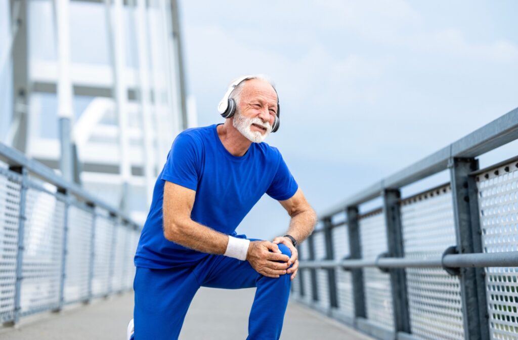 A senior stops mid-run, clutching their knee in discomfort.