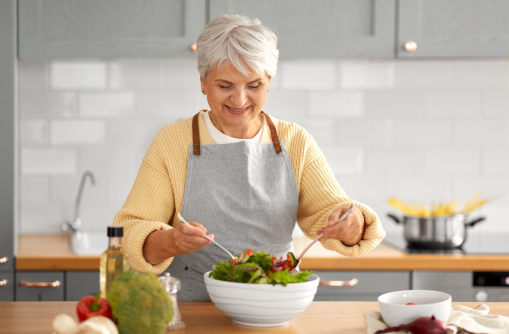 A senior woman preparing a bowl of salad in the kitchen.