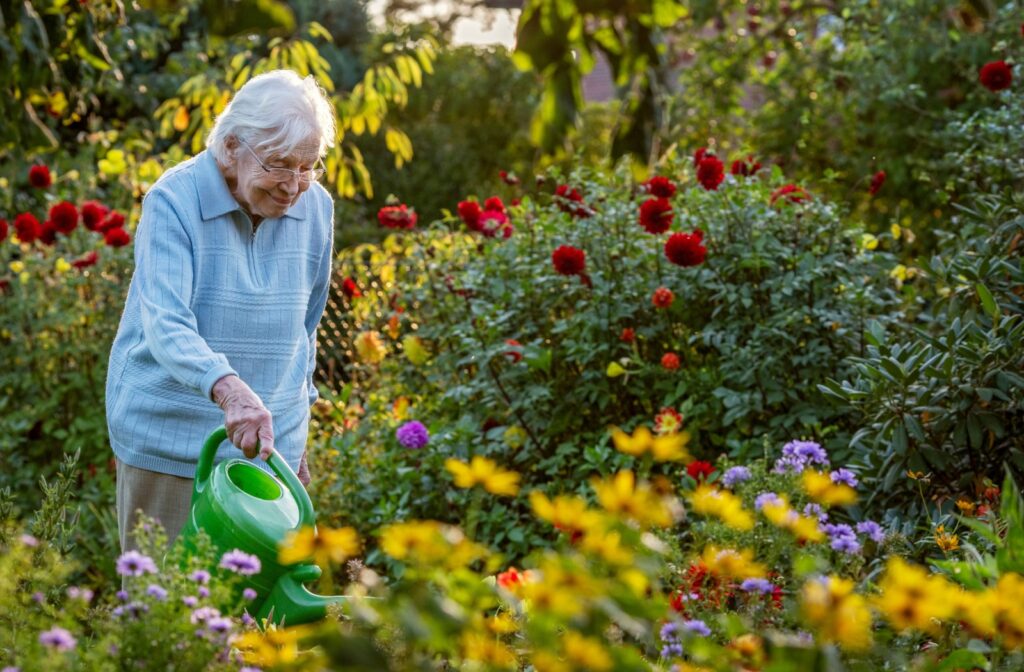 A happy older adult woman watering the plants of the independent living home.