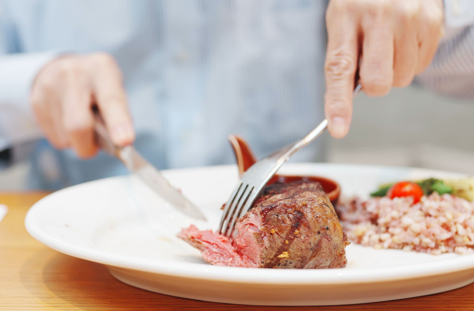 A person eating prime rib, vegetables, and rice for dinner.