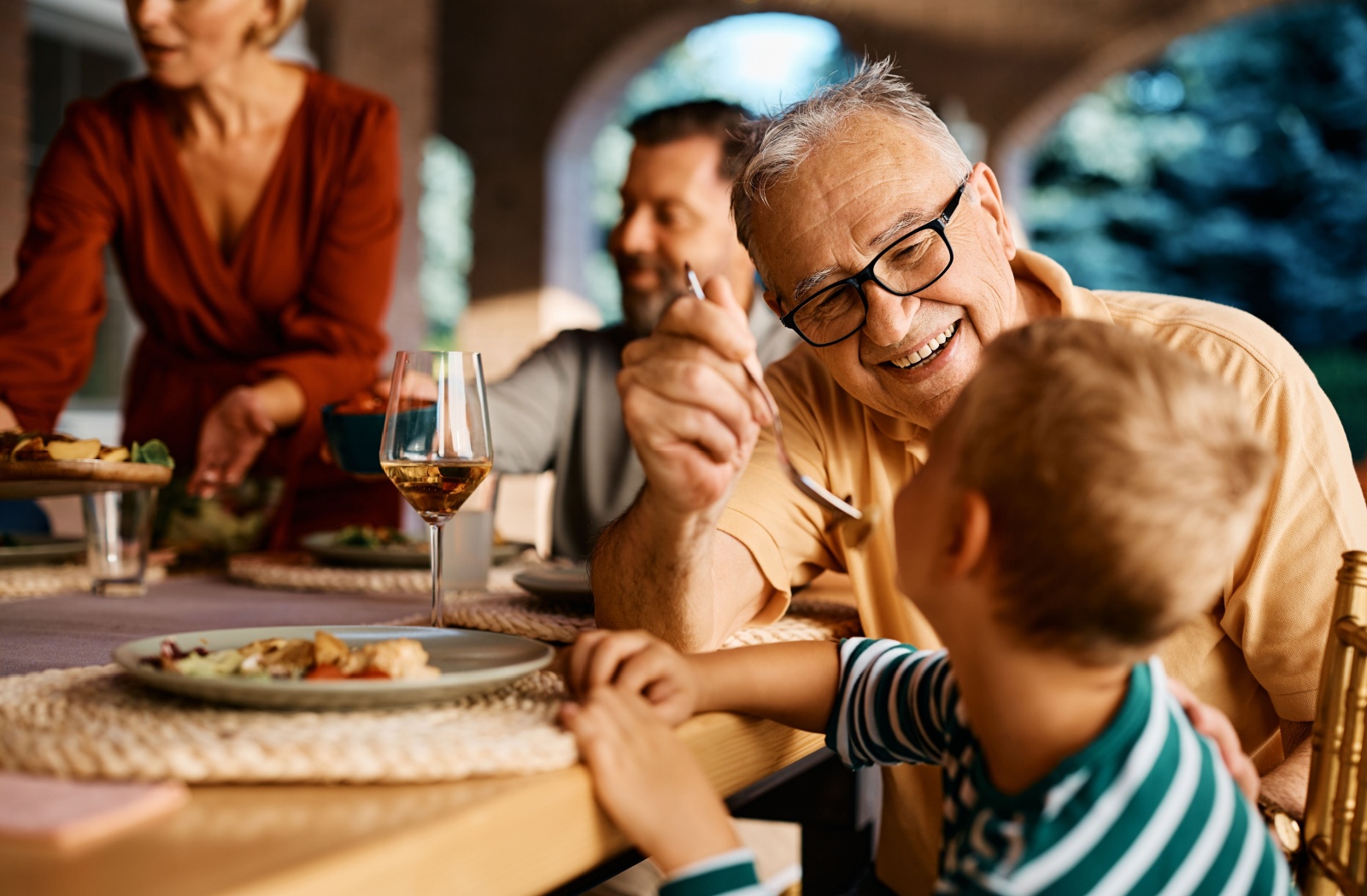 Older man feeding grandson at dinner.