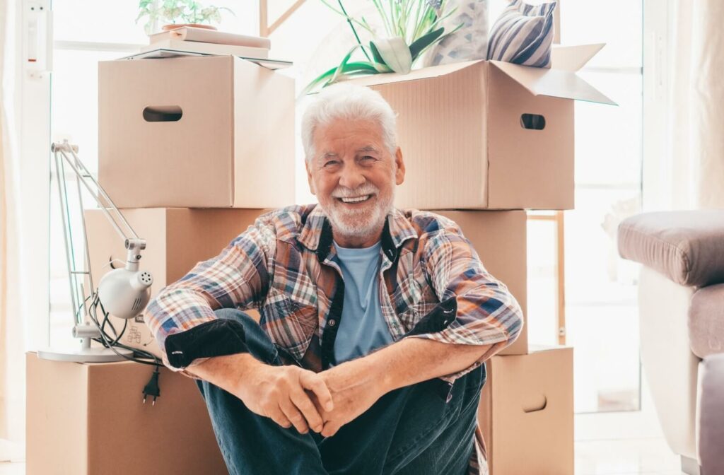 Smiling senior adult sitting on the floor surrounded by moving boxes.