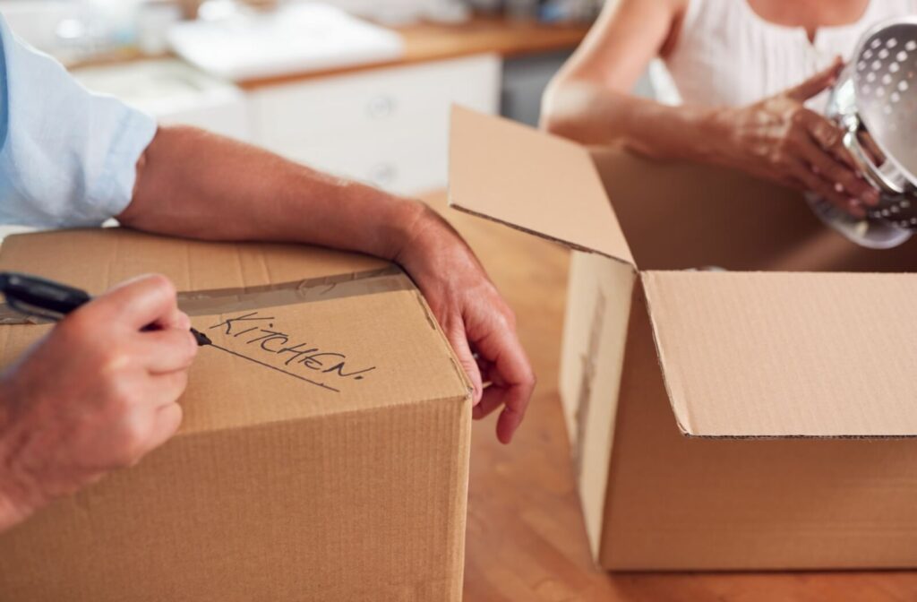 Close-up of a person labeling a moving box with 'Kitchen' while packing.