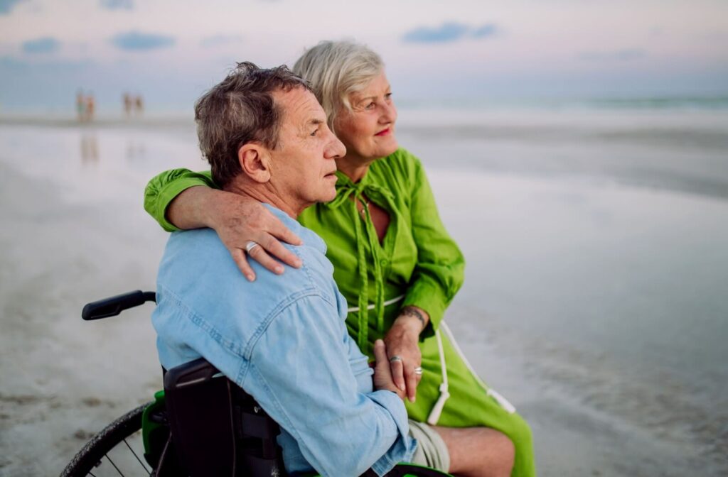 A senior sitting in a wheelchair with their partner sitting on their lap gazes at the sea.