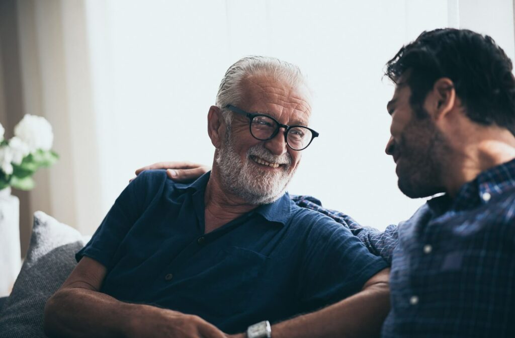 An older adult smiling and looking at their adult child while talking together during a visit.