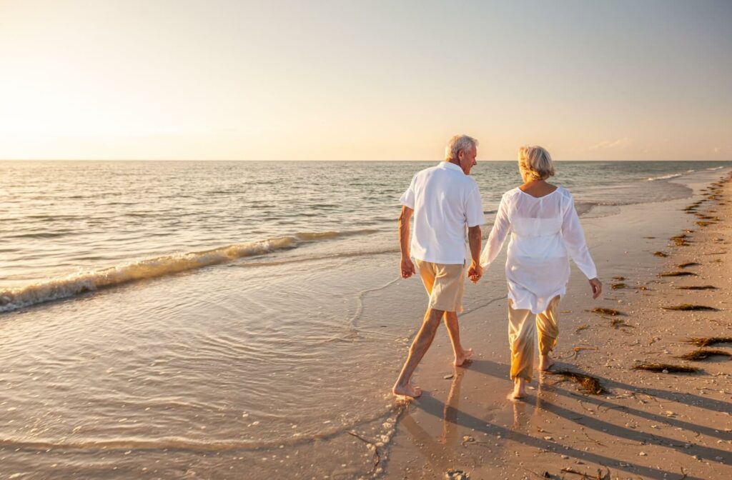 two seniors holding hands and walking in the beach