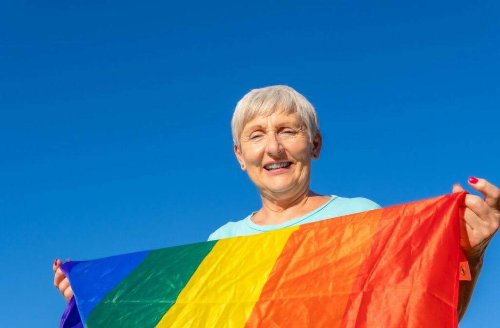 A senior smiles as they hold up a pride flag.