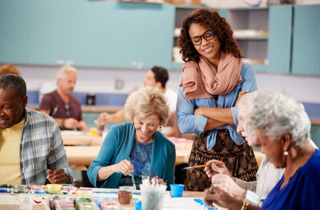 An art teacher is looking at what a group of seniors in their art class are painting.