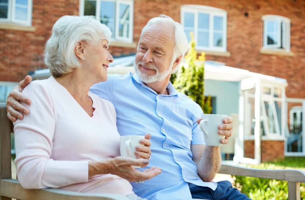Two older adults sit outside and share a nice moment together while drinking coffee in the courtyard of their independent living community