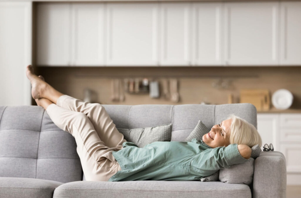 An older adult lies on their couch and smiles up at the ceiling while relaxing in their new home in independent living