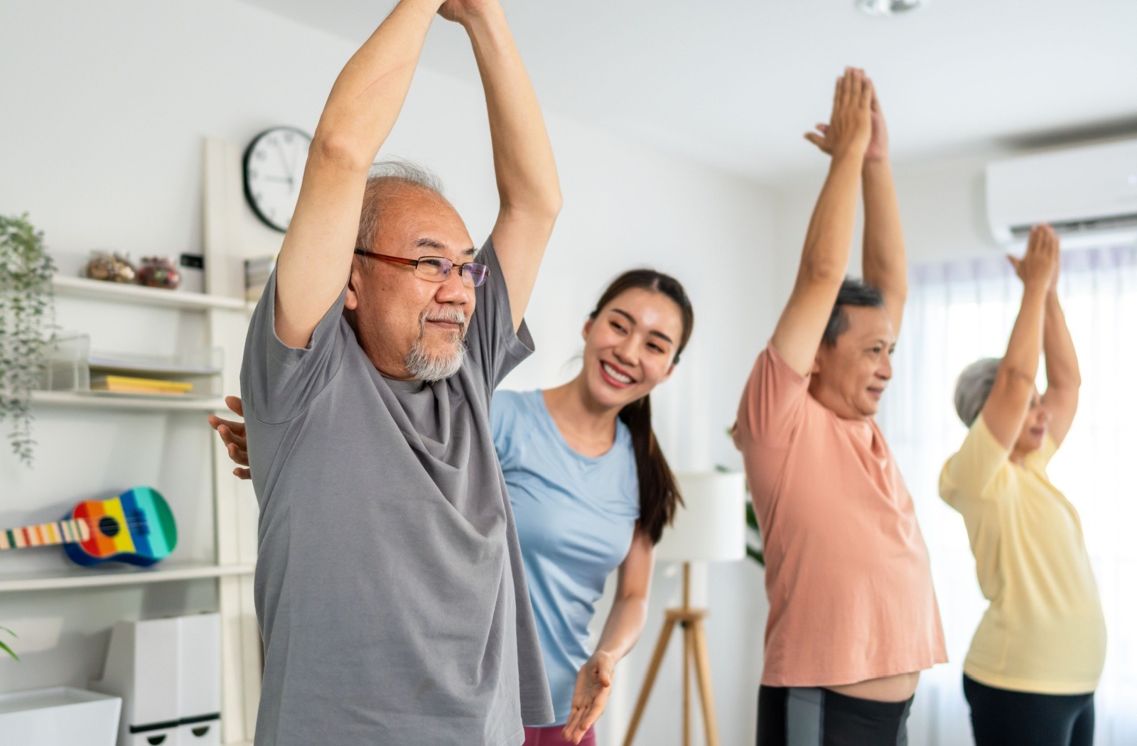 A group of seniors perform yoga poses under the guidance of a personal trainer.
